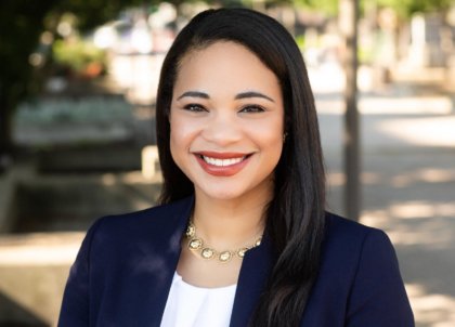 Photo of woman with dark hair wearing navy blue blazer smiling at camera