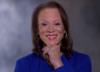 Photo of woman with short dark hair holding hand up to chin and smiling at camera