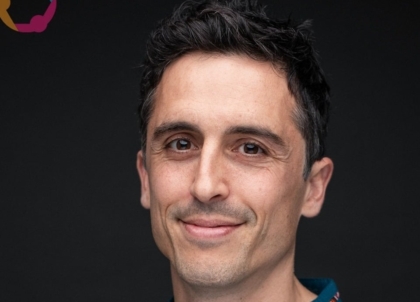 Photo of man with short dark hair wearing blue shirt with red stripe smiling at camera