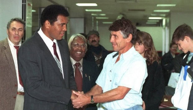 Muhammad Ali shakes hands with a man, a crowd looks on