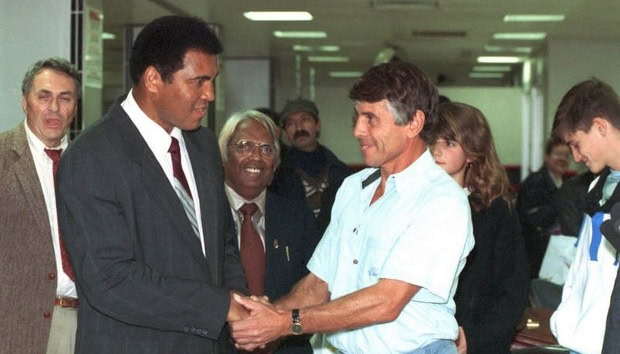 Muhammad Ali shakes hands with a man, a crowd looks on