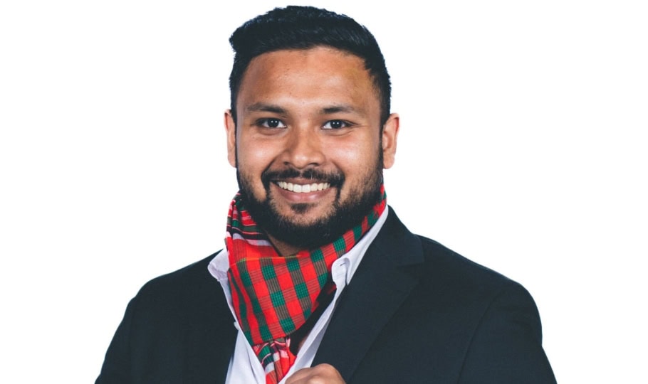 Photo of young man with short dark hair and beard wearing suit and posing for camera