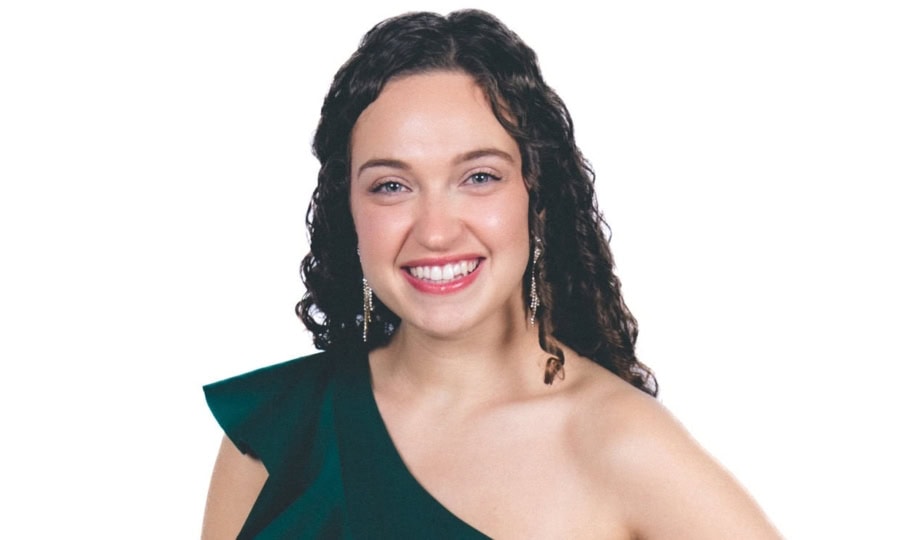 Photo of woman with brown curly hair wearing green dress smiling at camera