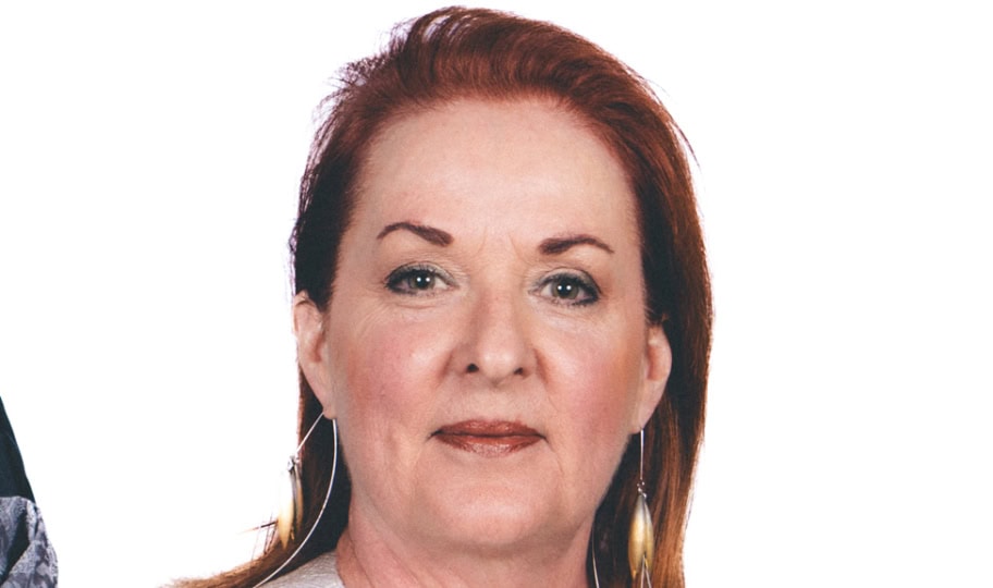 Photo of woman with shoulder-length red hair wearing silver-patterned jacket posing for camera