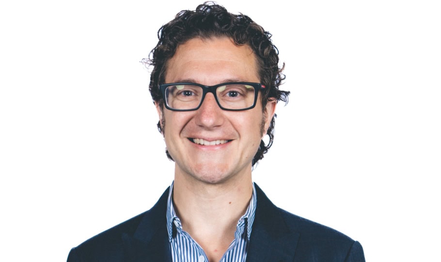 Photo of man with short curly hair and glasses wearing suit smiling at camera