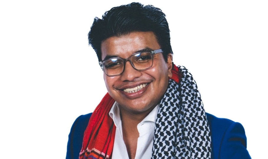 Photo of young man with dark hair, glasses and blue suit posing for camear