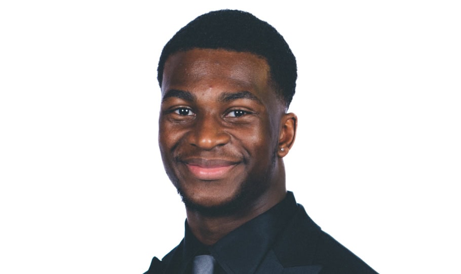 Photo of man with short dark hair wearing black suit and silver tie smiling at camera