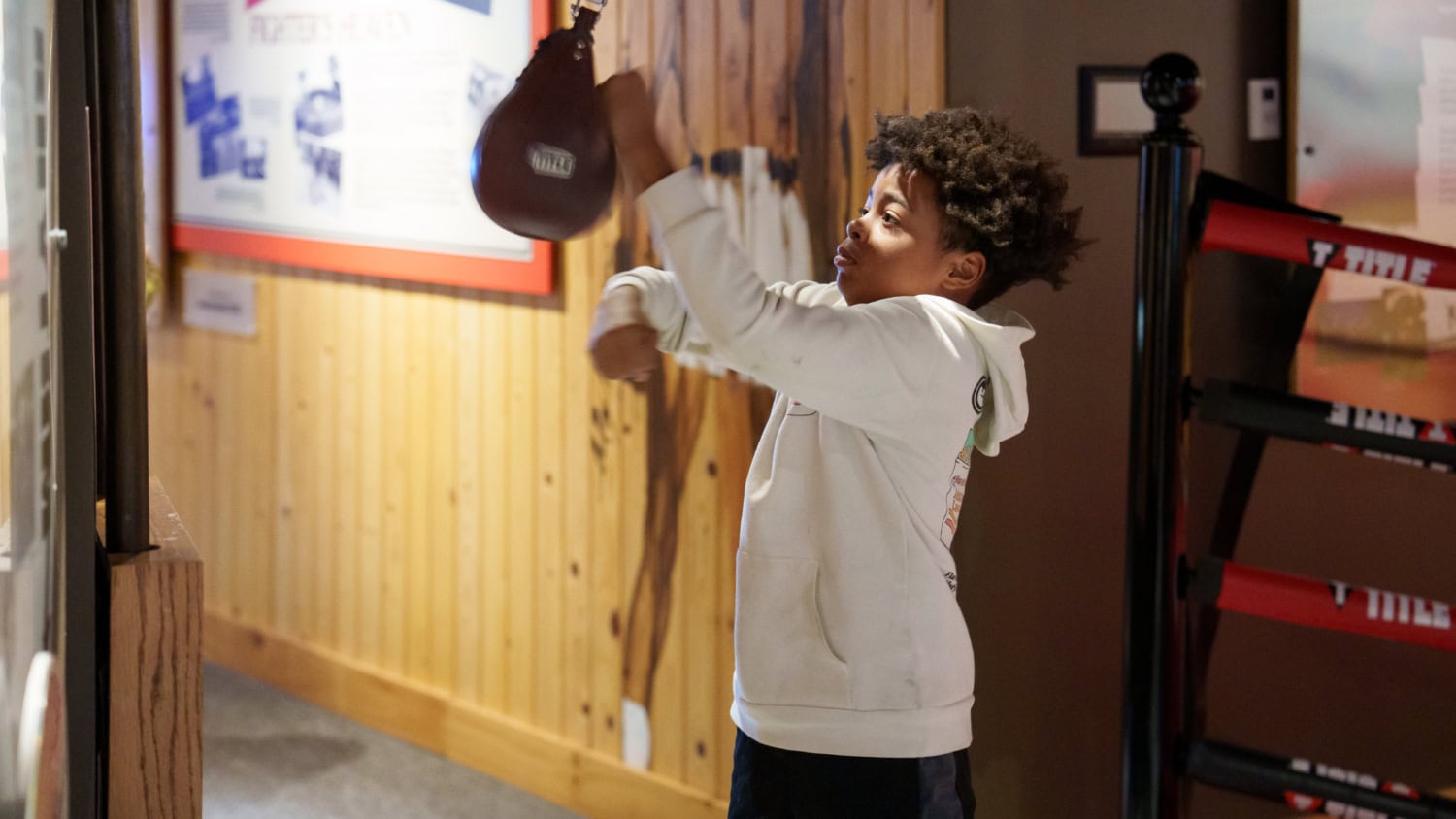 Kid in white sweatshirt hitting speedbag in Ali Center's Deer Lake exhibit