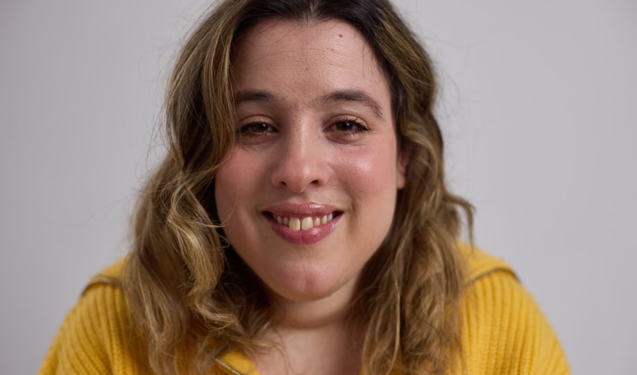 Woman with shoulder-length brown hair wearing yellow sweater smiling at camera