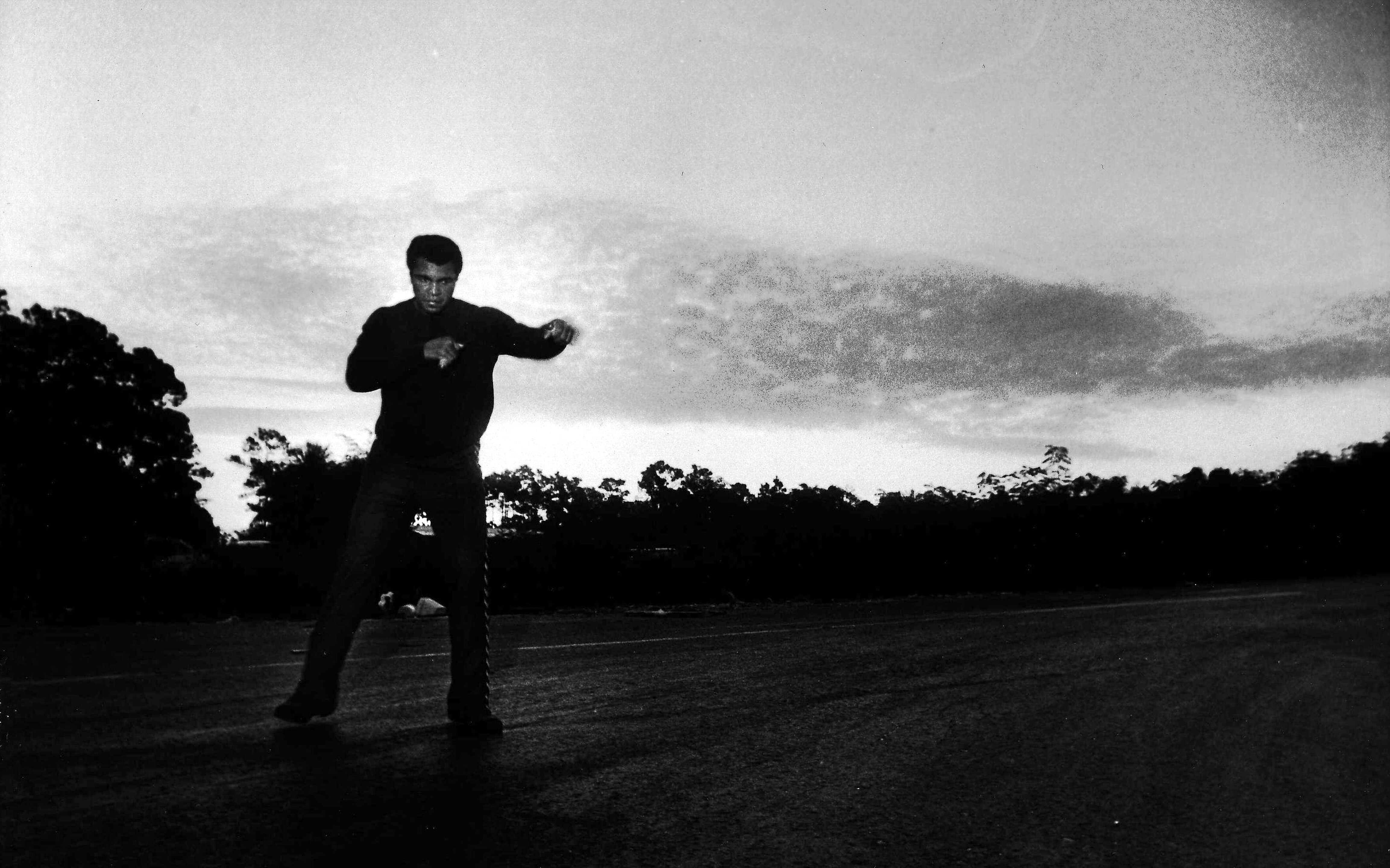 Black and white photo of Muhammad Ali in a boxing stance outside near skyline