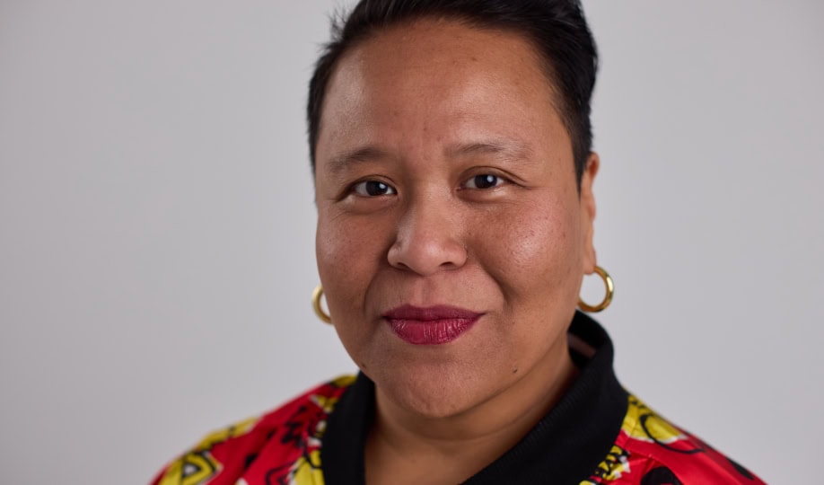 Woman wearing red and yellow top and gold earrings smiles at camera