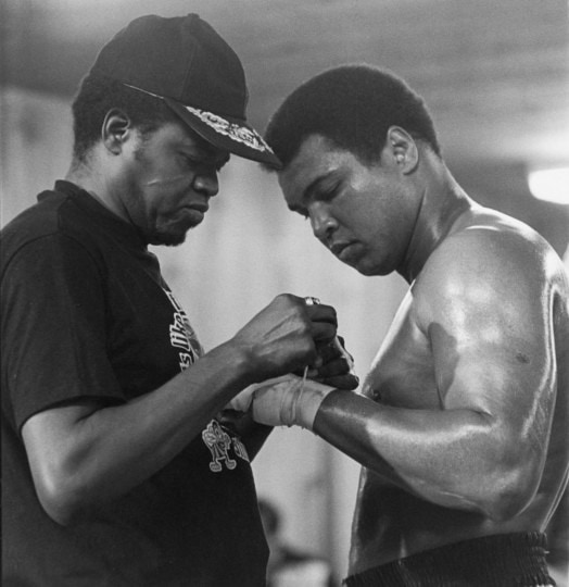 Muhammad Ali, in boxing shorts, having his hand taped