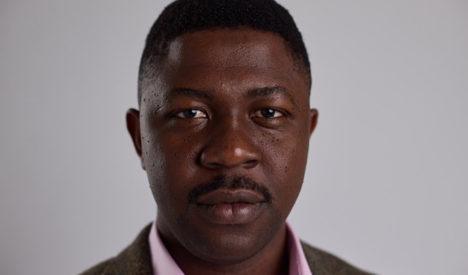 Man with short dark hair and moustache wearing suit jacket looks at camera