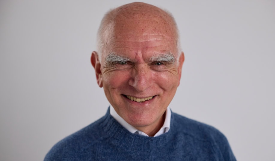 Photo of older gentleman wearing button-up and blue sweater smiling at camera