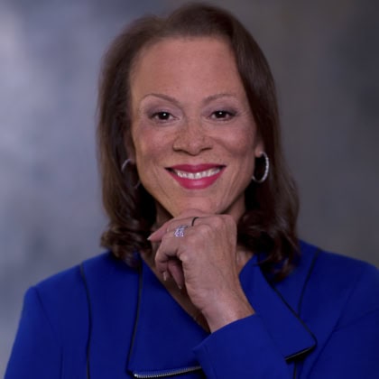 Photo of woman with short dark hair holding hand up to chin and smiling at camera