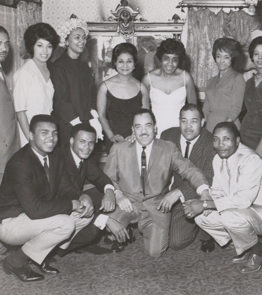 Black and white photo of Muhammad Ali sitting with group of people