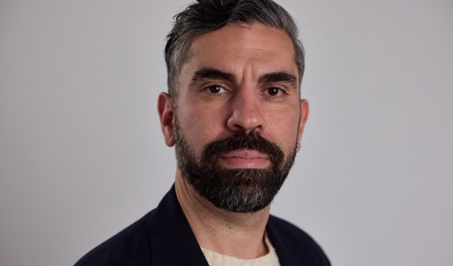 Photo of man with dark gray hair and beard wearing black sweater smiling at camera