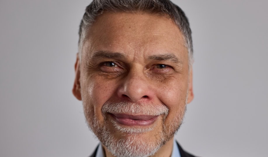 Man with short gray hair and white beard wearing suit jacket smiles at camera