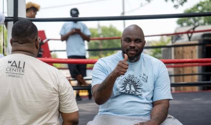 A man sits on the side of a boxing ring and gives a thumbs up