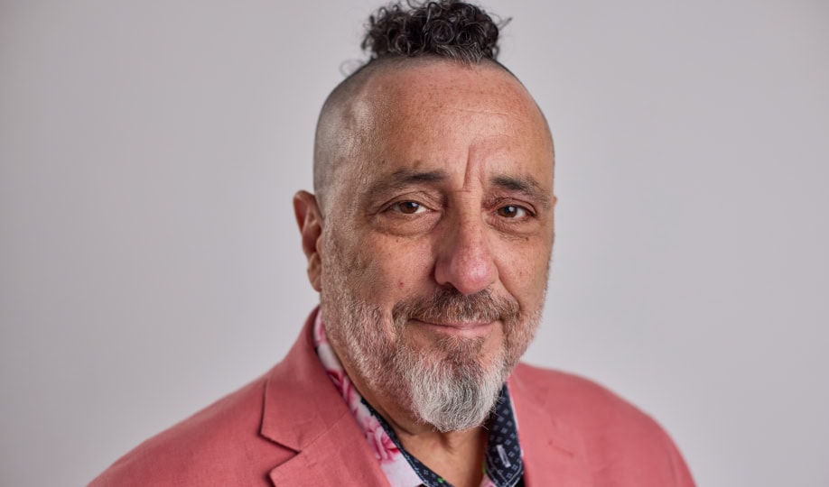 Photo of man with short gray hair and beard wearing pink jacket smiling to camera