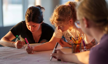 Three university students sitting at table drawing as sun beams down on them