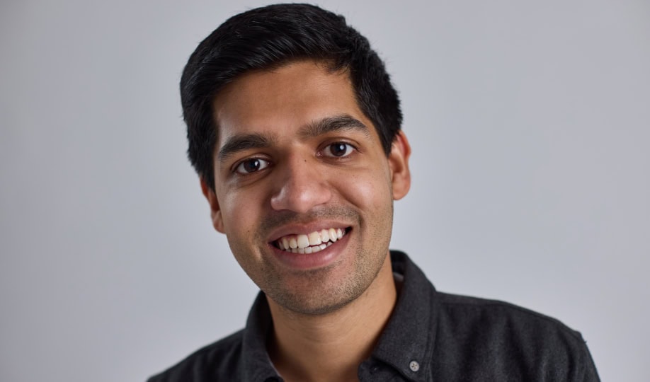 Photo of man with short dark hair wearing white shirt and gray jacket smiling at camera