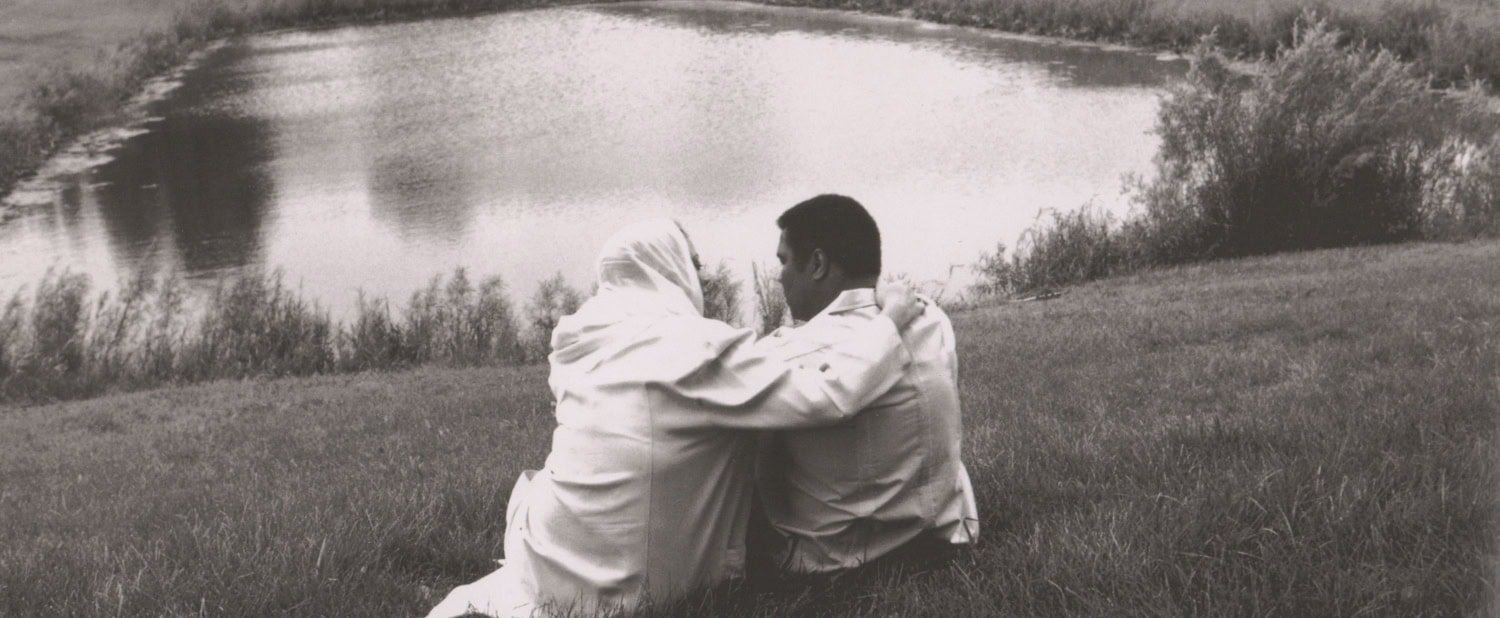 Black and white photo of Muhammad Ali and Lonnie from behind sitting at lake