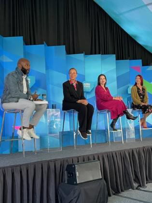 Four panelists discussing on stage in front of multi-colored background