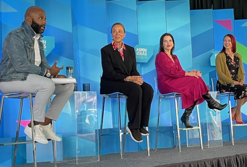 Four panelists discussing on stage in front of multi-colored background