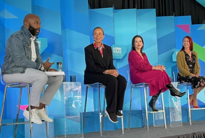 Four panelists discussing on stage in front of multi-colored background
