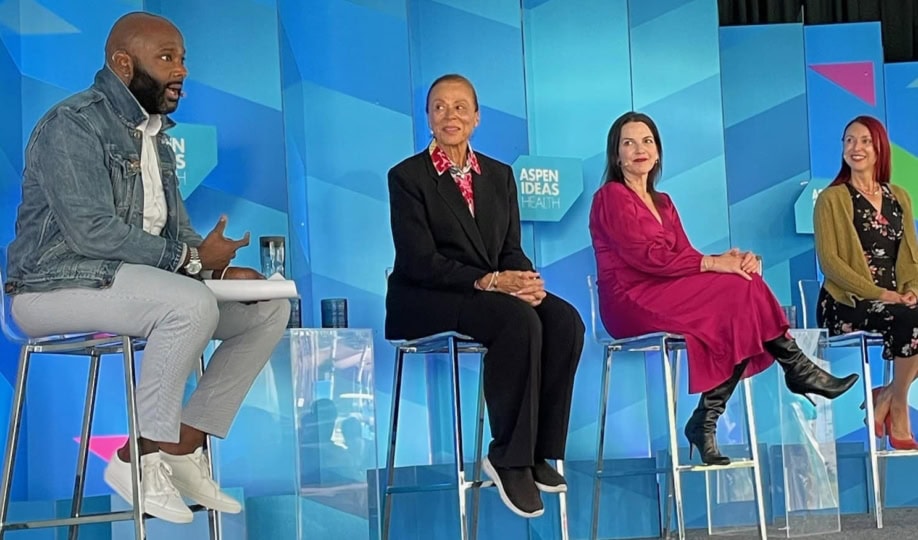 Four panelists discussing on stage in front of multi-colored background
