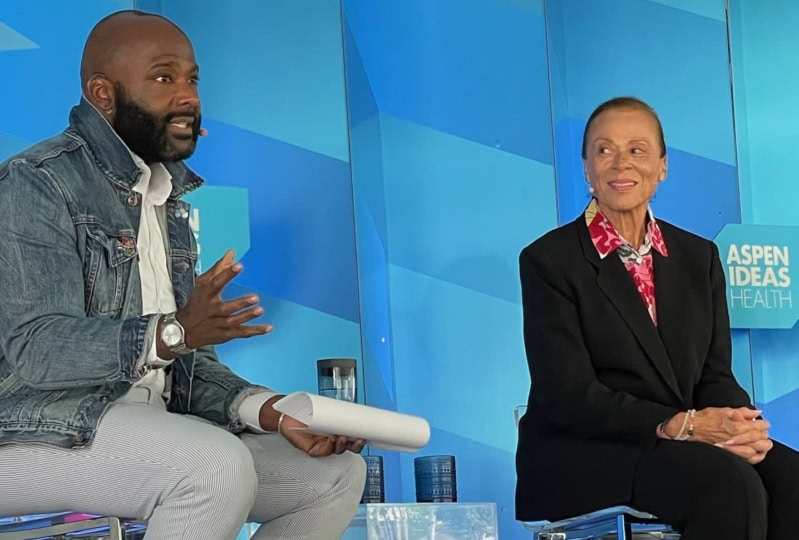 Lonnie Ali and Frederick Riley sitting and talking during panel discussion in front of blue backdrop
