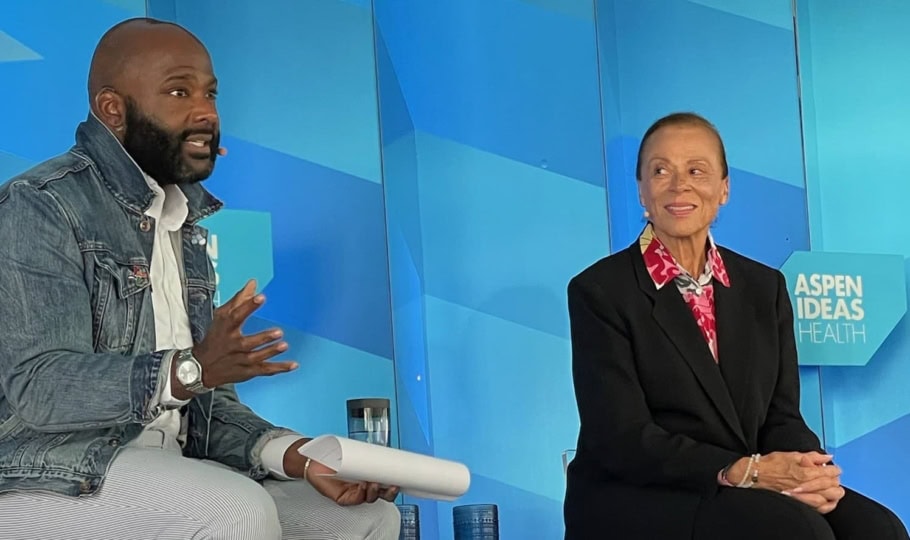Lonnie Ali and Frederick Riley sitting and talking during panel discussion in front of blue backdrop