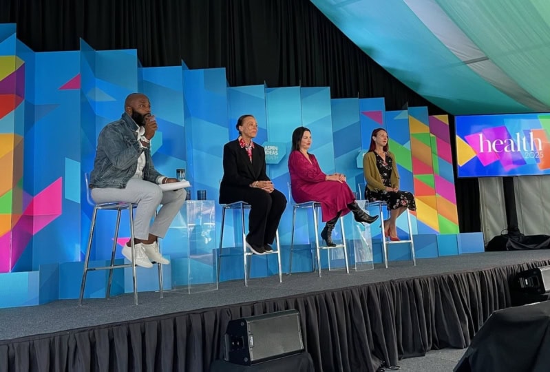 Four panelists discussing on stage in front of multi-colored background
