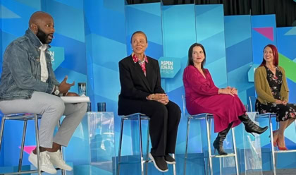 Four panelists discussing on stage in front of multi-colored background