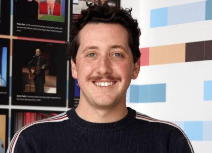 Picture of man with short curly hair and dark sweater smiling at camera