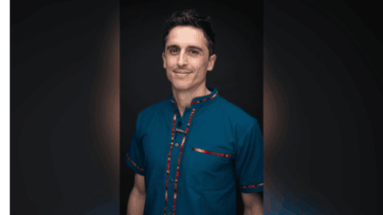 Photo of man with short dark hair wearing blue shirt with red stripe smiling at camera
