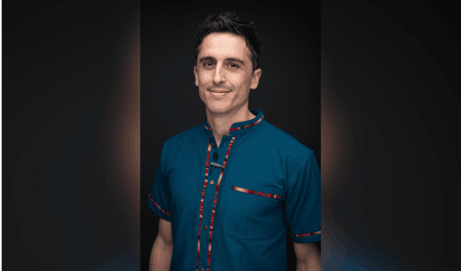Photo of man with short dark hair wearing blue shirt with red stripe smiling at camera