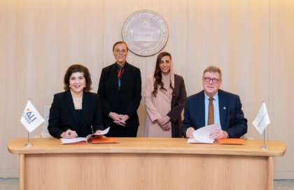 Four people sitting at wooden table and smiling at camera alongside flags with Muhammad Ali Center and American University of Sharjah logos