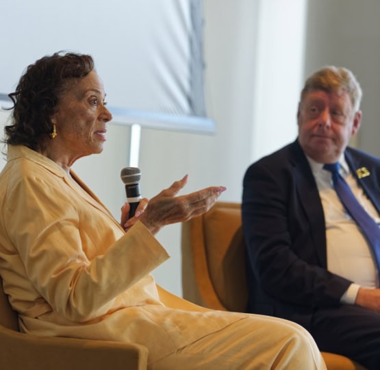 Woman in yellow suit and man in black suit with blue tie on a panel discussion
