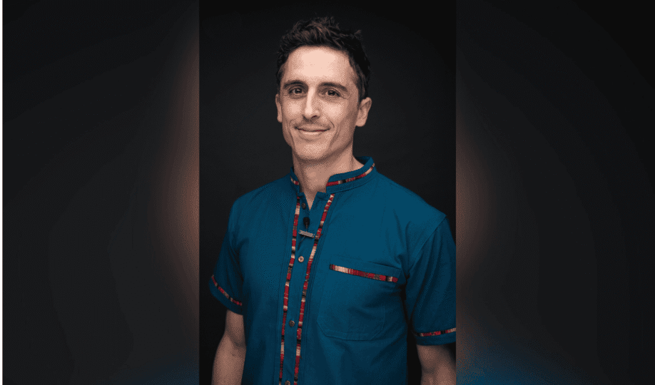 Photo of man with short dark hair wearing blue shirt with red stripe smiling at camera
