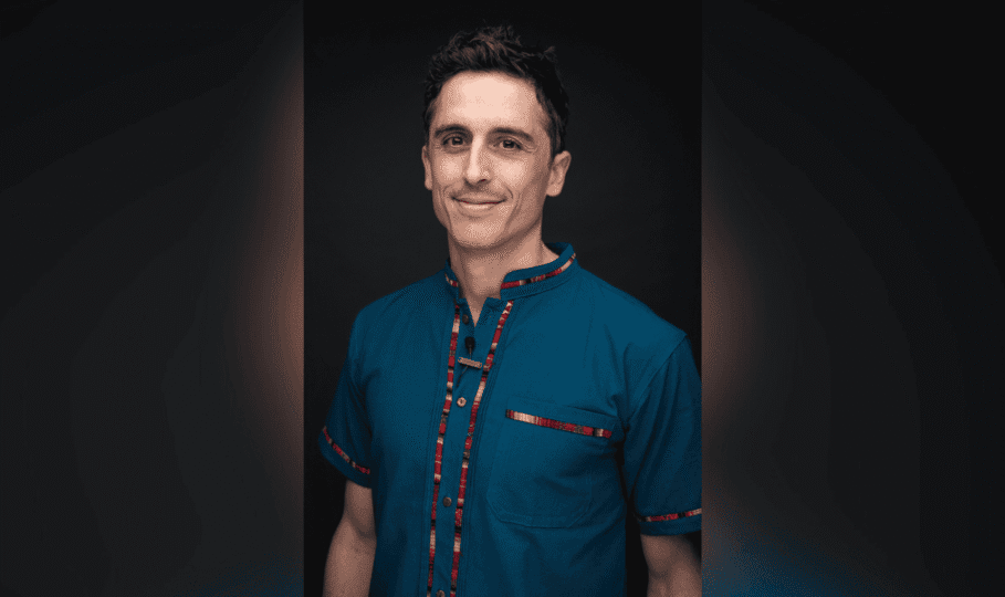 Photo of man with short dark hair wearing blue shirt with red stripe smiling at camera