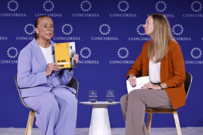 Lonnie Ali wearing purple suit sitting with woman wearing orange jacket and brown pants during panel discussion