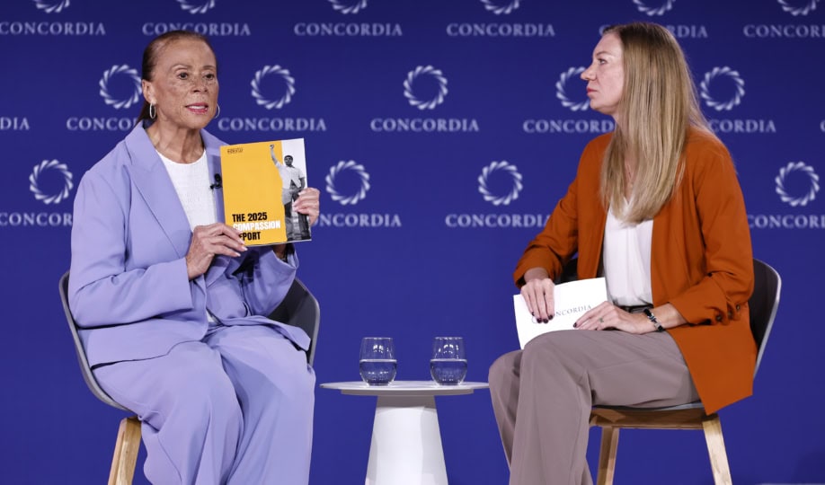 Lonnie Ali wearing purple suit sitting with woman wearing orange jacket and brown pants during panel discussion